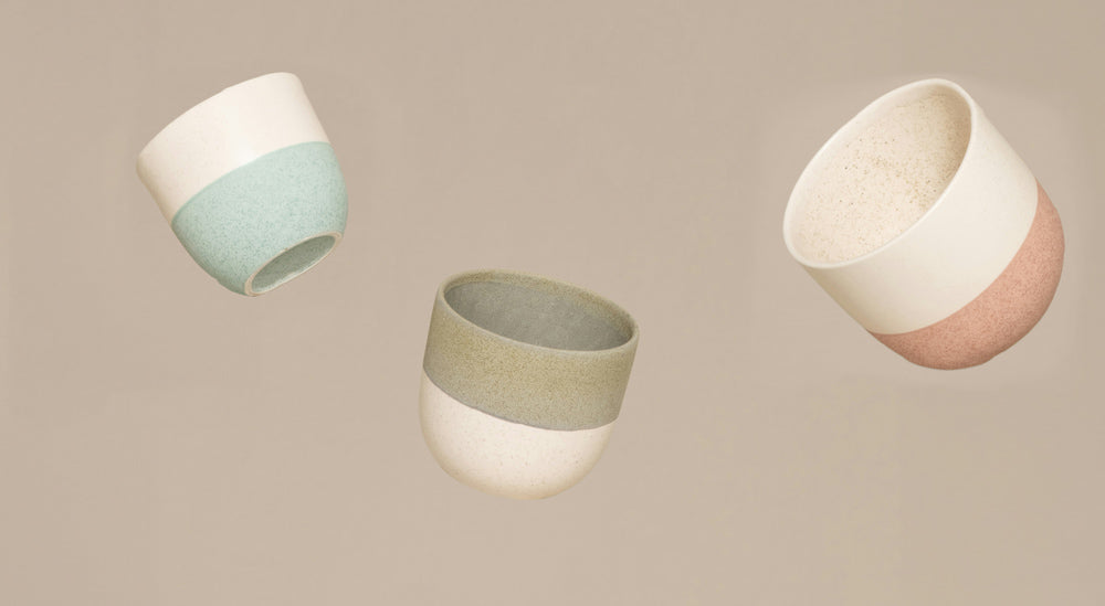 Drei Keramiktassen, jede mit einem zweifarbigen Design – Mintgrün, Olivgrün und Pink – schweben vor einem schlichten beigen Hintergrund.