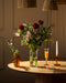 Ein prächtiger Blumenstrauß "Ich liebe Dich" mit roten Rosen auf einem runden Holztisch - begleitet von Orangensaft, weißer Kerze im bernsteinfarbenen Halter und Bernsteinvase - ein perfektes Geschenk, um Liebe auszudrücken.