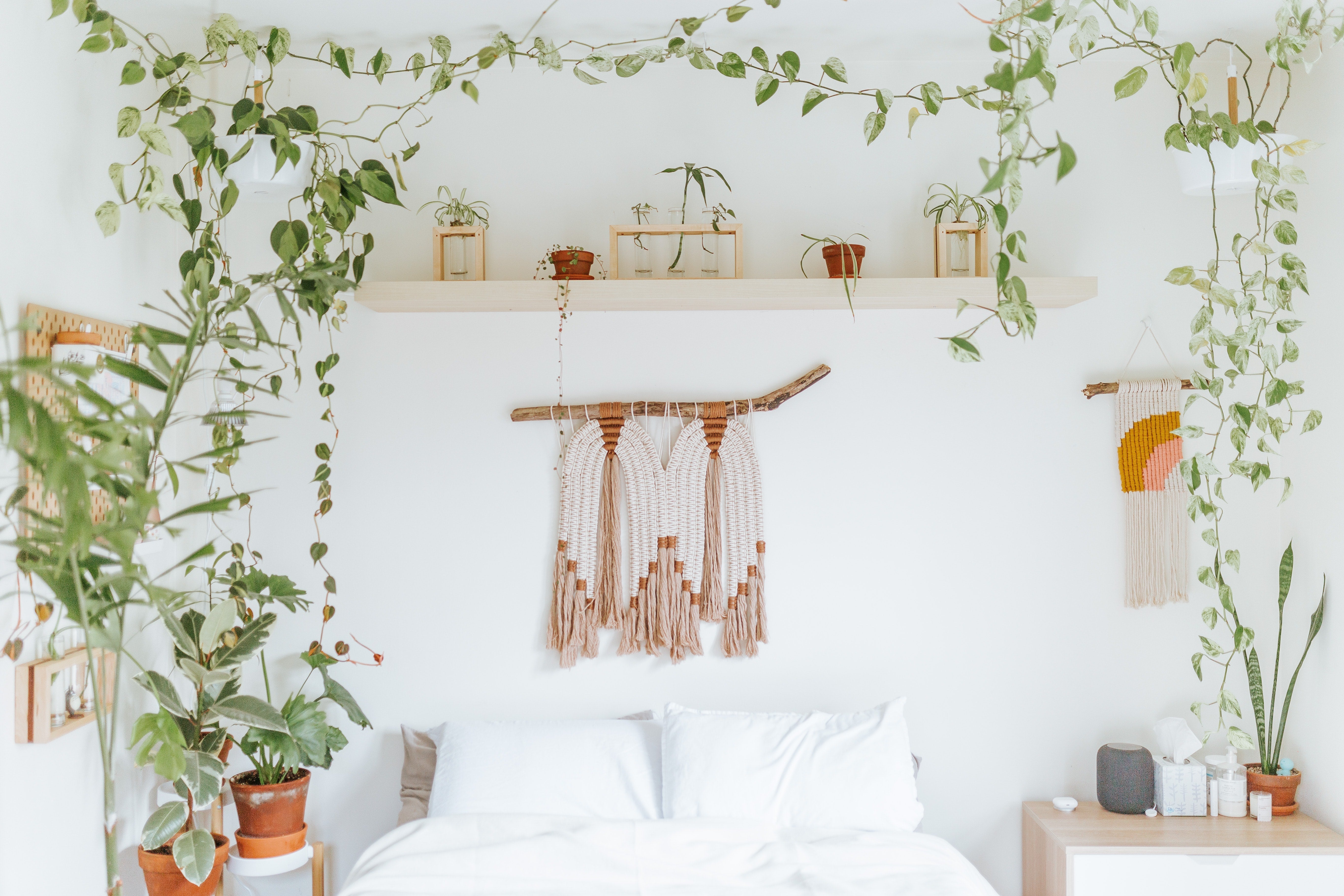 Schlafzimmer mit viel Weiss und Boho-Deko sowie diversen hängenden Zimmerpflanzen