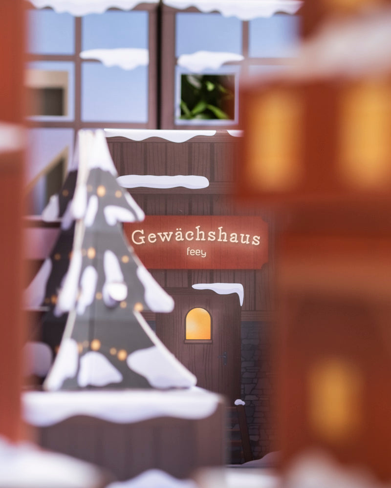 Eine gemütliche, verschneite Szene mit einem geschmückten Weihnachtsbaum und einem warm beleuchteten Gebäude mit einem 
