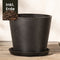 Ein großer schwarzer Kunststoff-Pflanzkübel (Amsterdam | 30 cm ⌀) mit passender Untertasse steht auf Holz - ideal für Ihren Balkon. Eine Einlage zeigt Erde mit "Inkl. Erde", was bedeutet, dass die Erde enthalten ist.