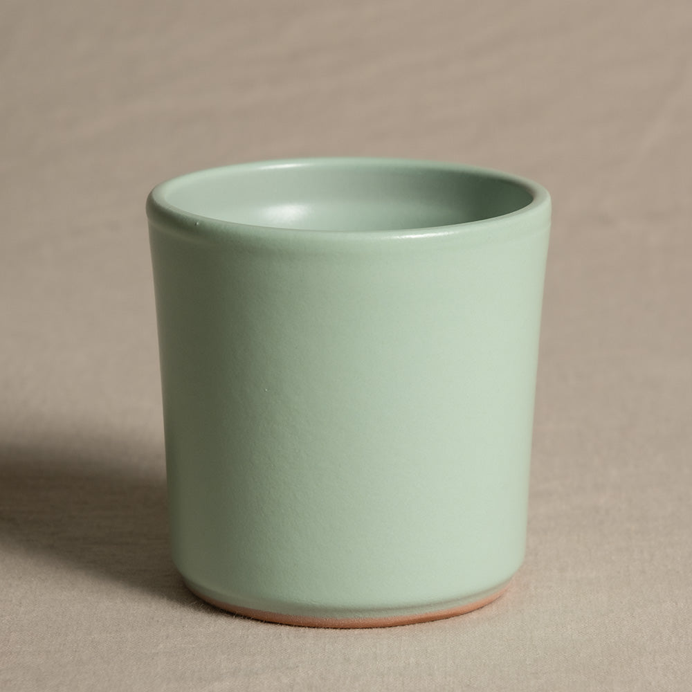 Eine kleine, mintgrüne Keramiktasse steht auf beigem Untergrund. Die Tasse hat eine glatte, matte Oberfläche und eine schlichte, zylindrische Form mit leicht abgerundeten Kanten. Ihr minimalistisches Design verleiht ihr ein modernes und elegantes Aussehen und macht sie perfekt als Keramik Babypflanzen-Topf 'Sencillo' für Feey-Babypflanzen.