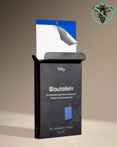 Eine offene schwarze Box mit der Aufschrift „Blautafeln gegen Thripse“ zeigt im Inneren eine blaue Klebefalle. Die aufrecht stehende Box ist ideal zur Überwachung von Thripsen und Schädlingsbefall und steht auf einer beigen Fläche vor neutralem Hintergrund.