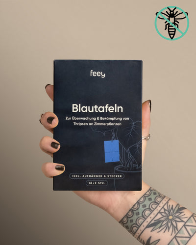 Eine tätowierte Hand mit schwarzen Nägeln hält vor beigem Hintergrund eine Schachtel mit der Aufschrift „Blautafeln gegen Thripse“ von feey. Eine Bienenillustration oben rechts deutet auf den Schutz vor Schädlingen wie Thripse hin.