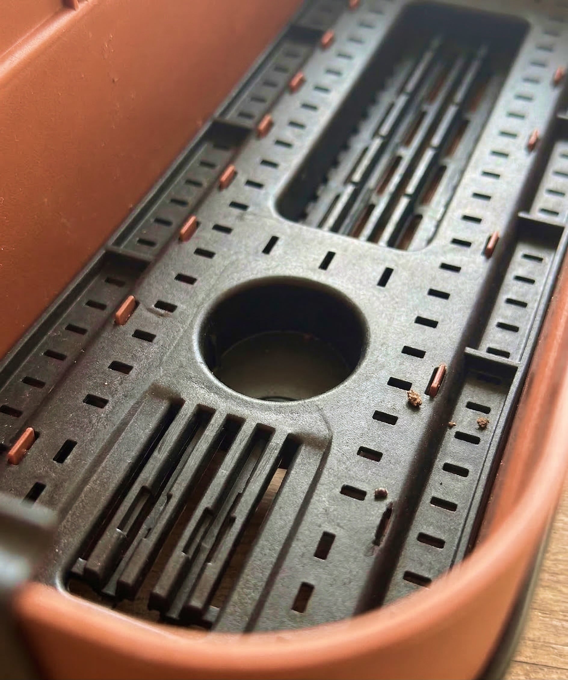 Nahaufnahme des Pflanzkastens für Geländer (Blossom | 60 cm) in Braun und Schwarz, mit einem geschlitzten Tablett-Einsatz und einem kreisrunden Fach in der Mitte, ideal für die Entwässerung oder Abtrennung auf Ihrem Balkon.