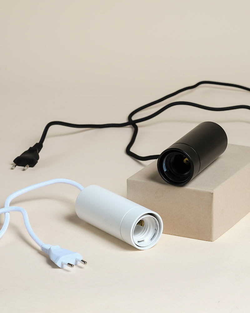 Zwei Pendelleuchten 'Corda' - eine schwarze auf einem beigen Block, eine weiße auf einer flachen Oberfläche - jeweils mit passender Schnur und Stecker. Perfekt als Pendel- oder Pflanzenlampen, um Zimmerpflanzen zu präsentieren.