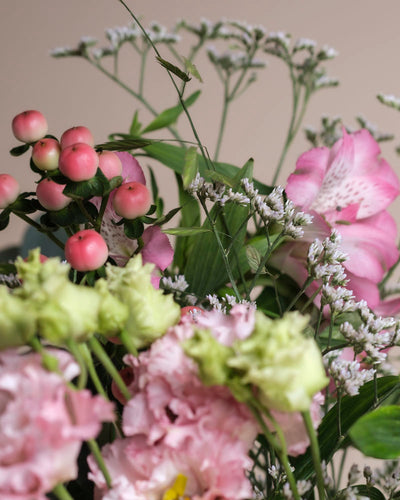 Eine Nahaufnahme des Ballerina-Straußes mit rosa und grünen Blüten, kleinen runden rosa Beeren und zarten weißen Füllblumen vor einem neutralen Hintergrund.