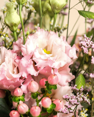 Eine Nahaufnahme von Morgenlicht, einem handgebundenen Blumenarrangement mit zartrosa Lisianthus, rosa Beeren, lila Blüten und grünen Akzenten - perfekt für Ihr Zuhause.