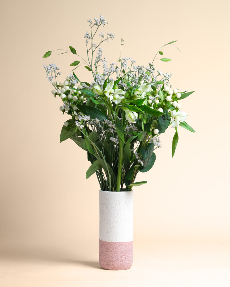 In einer weiß-rosafarbenen Keramikvase steht der Luftkuss-Strauß aus grünen Blattstielen und kleinen weißen Blüten vor einem hellbeigen Hintergrund, der wie ein luftiger Kuss einen zarten Hauch von Liebe vermittelt.