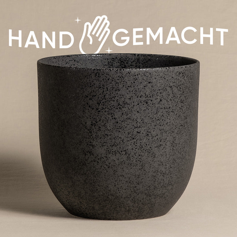 Ein strukturierter, dunkelgrauer, heller Keramik-Topf (Direito | 22 cm ⌀) ist zentriert vor einem neutralen Hintergrund platziert. Das deutsche Wort „HANDGEMACHT“ steht in Weiß oben, begleitet von einem Symbol einer Hand mit Glitzer.
