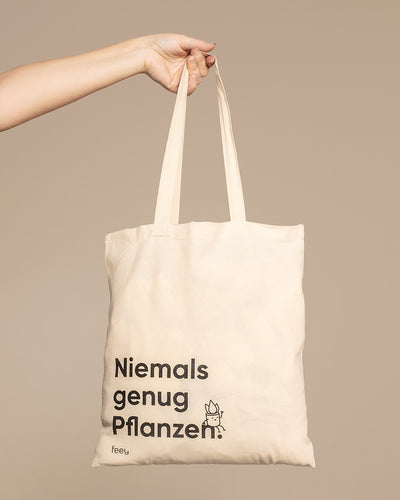 Hand hält eine Stofftasche mit dem Aufdruck «Niemals genug Pflanzen» 