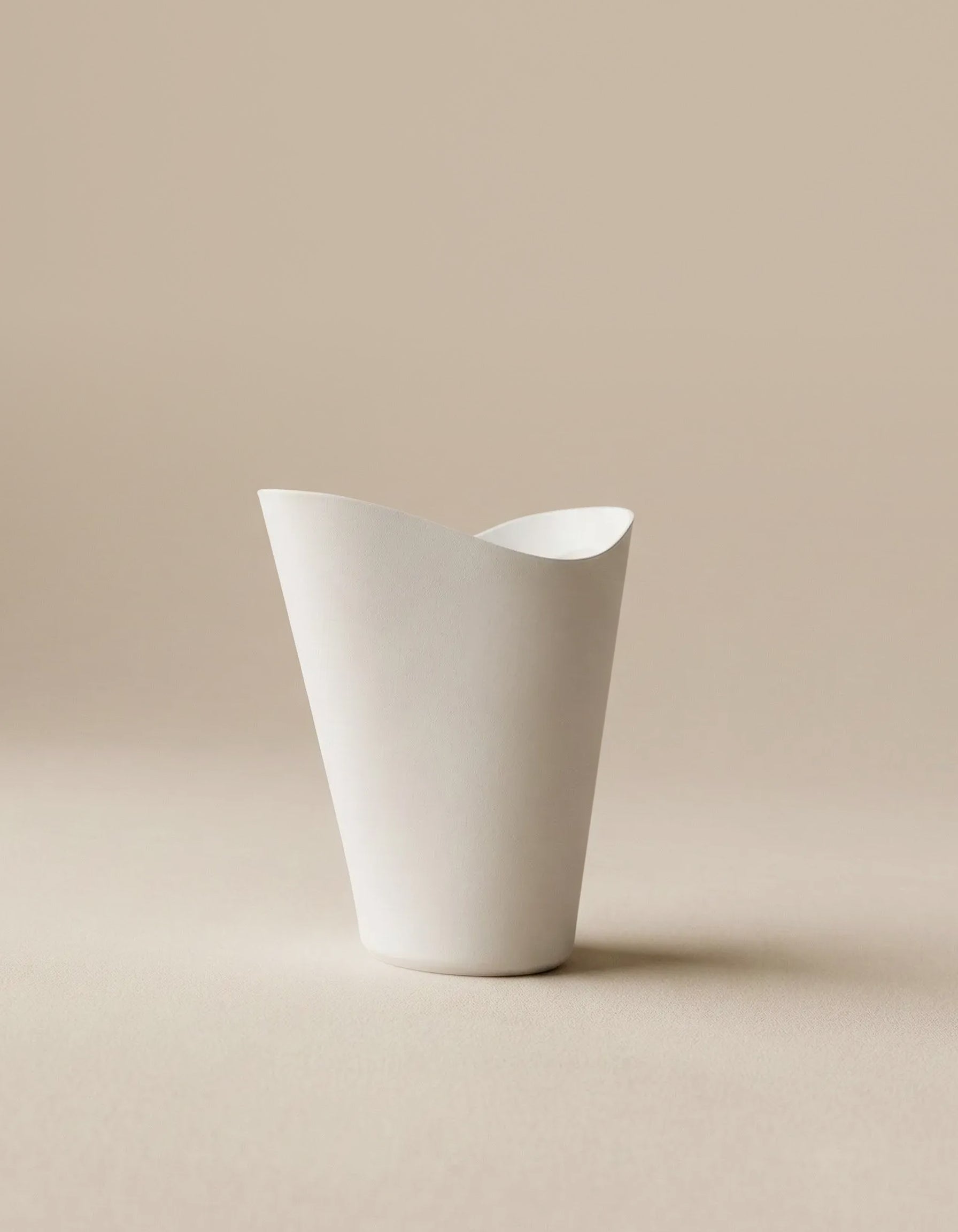 Der Giessbecher für Babypflanzen, ein minimalistischer weisser Messbecher mit asymmetrischem Design und geschwungenem Rand, steht auf einer beigen Fläche - ideal zum genauen Abmessen der Wassermenge bei der Pflege von Jungpflanzen.