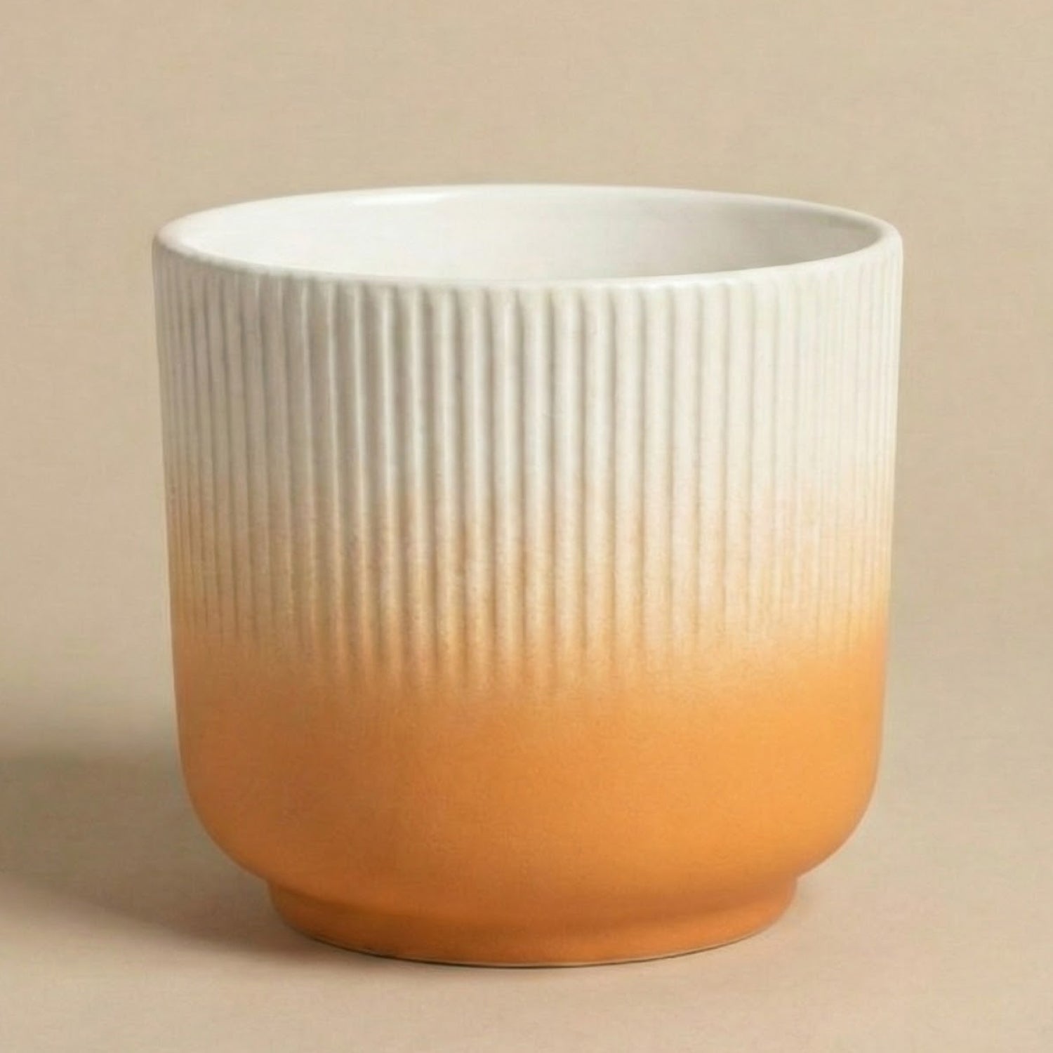 Der feey Keramik-Topf (Rilio | 14 cm ø) zeichnet sich durch vertikale Rillen und einen sanften Farbverlauf von weiß oben nach orange unten aus, der auf einem einfarbig beigen Hintergrund dargestellt ist.