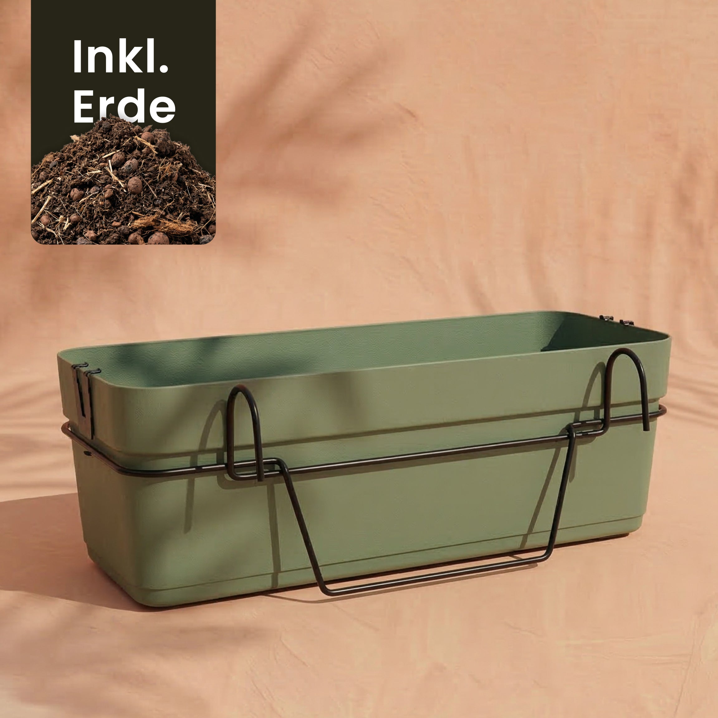 Ein grüner Pflanzkasten für Geländer (Blossom | 60 cm) mit Wasserreservoir steht auf schwarzem Metallständer vor pfirsichfarbener Kulisse. Ecke mit Erde und 