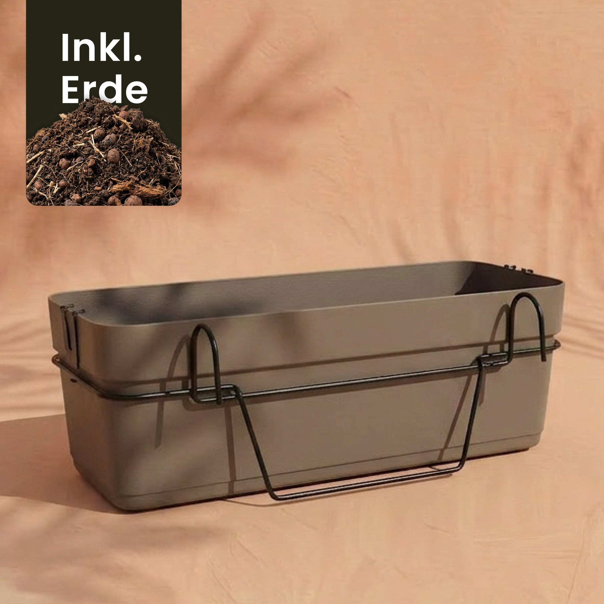 Ein rechteckiger taupefarbener Pflanzkasten für Geländer (Blossom | 60 cm) mit schwarzem Metallhalter ist auf einem pfirsichfarbenen Hintergrund abgebildet. Ein Einsatz zeigt Erde mit 