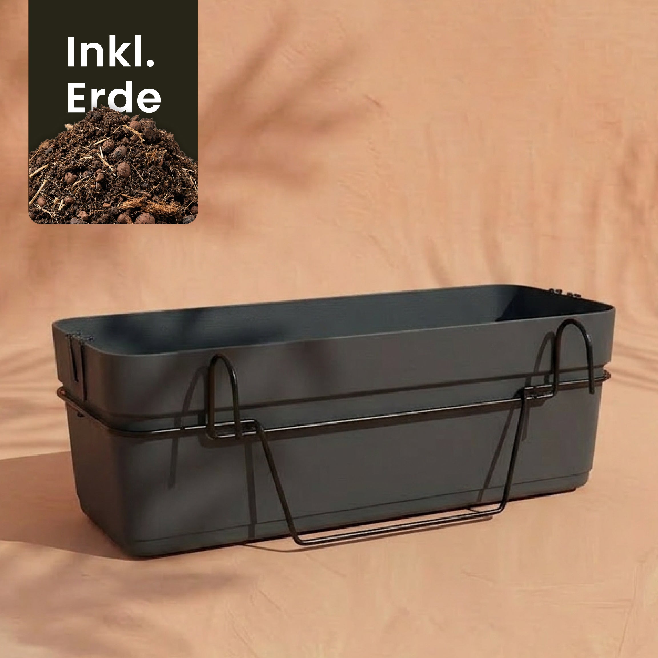 Ein rechteckiger dunkelgrauer Pflanzkasten für Geländer (Blossom | 60 cm) mit einem Metallhalter steht vor einem pfirsichfarbenen Hintergrund. 