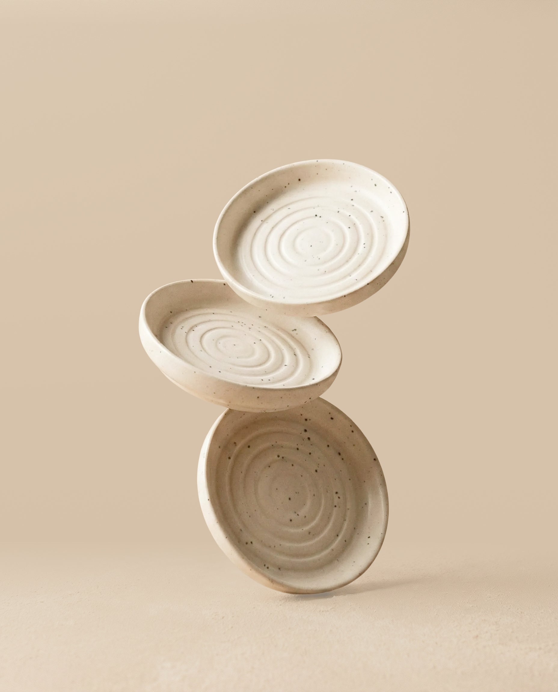 Drei Babypflanzen-Untersetzer aus Keramik (Plattino | 3 Stk.) in Creme, jeweils mit konzentrischen Kreismustern, sind in einer ausgewogenen Anordnung vor einem einfarbig beigen Hintergrund gestapelt.