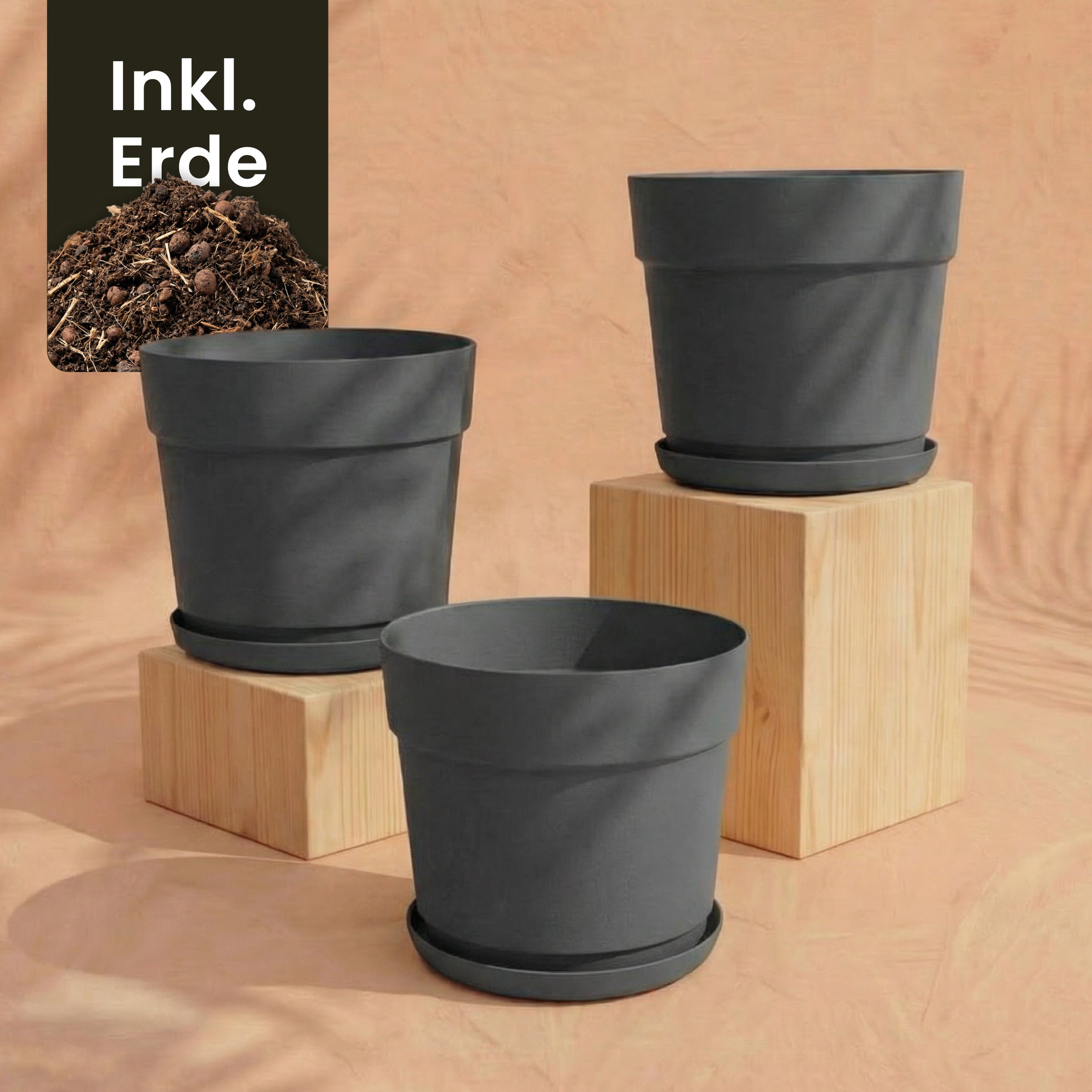 Das Pflanzkübel-Set 'Bloom' (3× 29) in schwarz mit passenden Untertassen ist auf Holzklötzen abgebildet, pfirsichfarbener Hintergrund. Hergestellt aus recyceltem Kunststoff, UV-beständig. Ein 