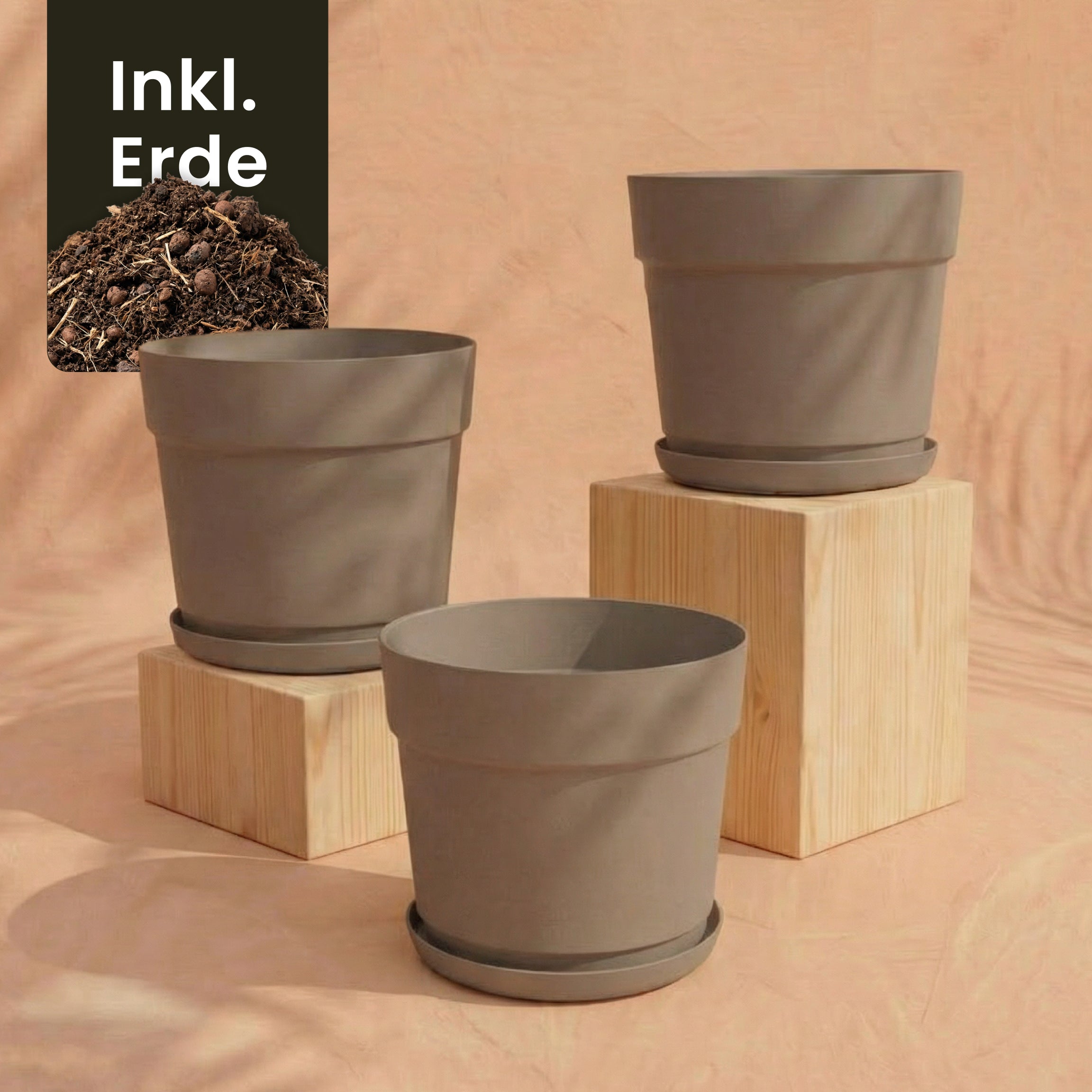 Drei taupefarbene Pflanzkübel aus recyceltem Kunststoff des Sets 'Bloom' (3×29) mit passenden Untersetzern stehen auf und neben Holzblöcken vor pfirsichfarbenem Hintergrund. Oben links ist ein 
