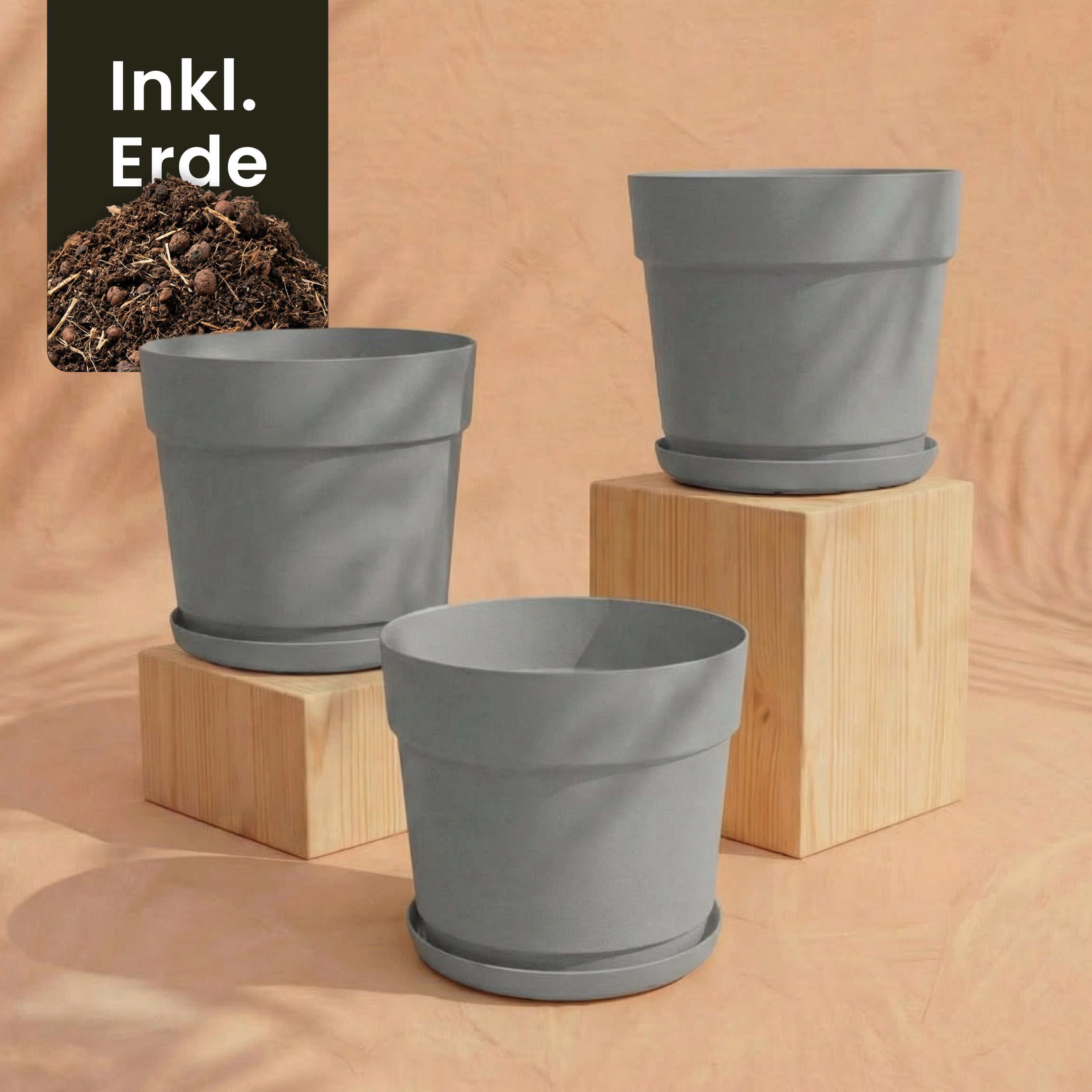 Drei graue Pflanzkübel-Set 'Bloom' (3× 29), aus recyceltem Kunststoff, mit passenden Untertassen sind auf Holzblöcken vor einem pfirsichfarbenen Hintergrund ausgestellt. Die Grafik oben links zeigt Erde und den Text 