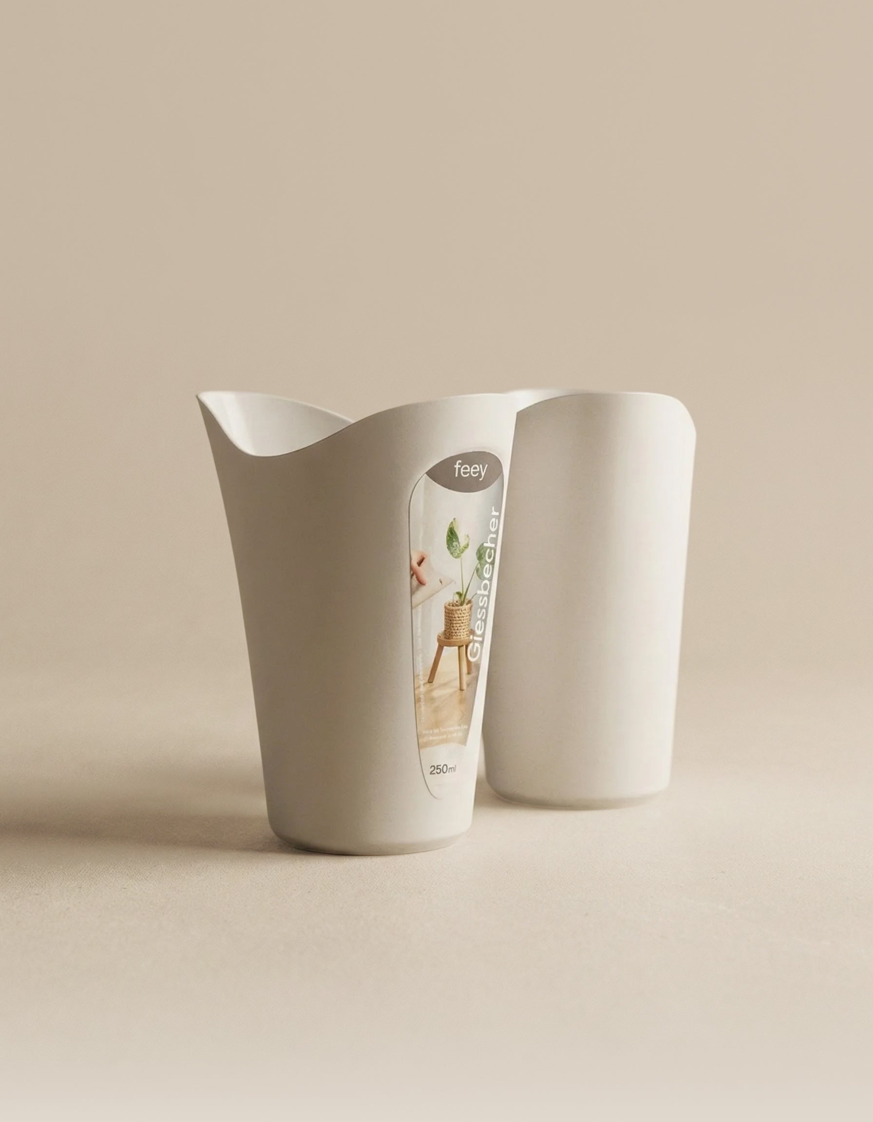 Zwei weiße, minimalistische Giessbecher für Babypflanzen stehen auf einer neutralen Oberfläche. Auf der Vorderseite befindet sich ein Feey-Logo mit Pflanzenmotiven und den Angaben 
