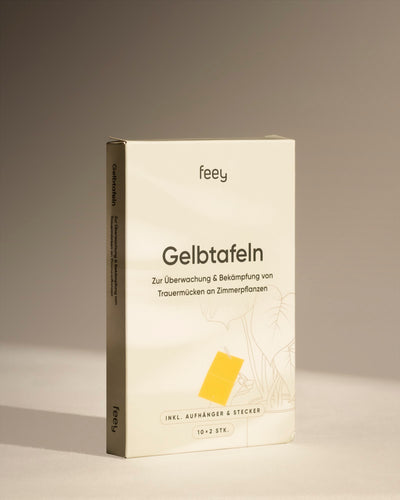 Eine Schachtel Gelbtafeln, klebrige gelbe Fallen zur Überwachung und Kontrolle von Trauermücken und zur Reduzierung von Schädlingen an Zimmerpflanzen, steht aufrecht vor einem neutralen beigen Hintergrund.