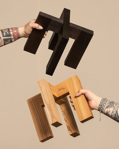 Tätowierte Unterarme halten ineinandergreifende Holzformen, wobei die Oberseite dunkelbraun und die Unterseite aus hellem Holz mit der Inschrift „feiy“ ist. Dieses minimalistische Design bildet einen eleganten Kontrast zu einem schlichten beigen Hintergrund und spiegelt die Handwerkskunst des Pflanzenständers (Heviton | 25 cm Ø) wider.