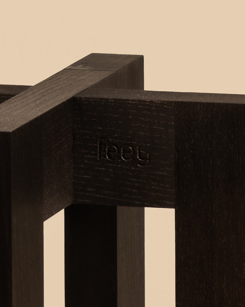Eine Nahaufnahme einer dunklen Holzstruktur mit minimalistischem Design, auf der „fleey“ eingraviert ist. Dieser elegante Pflanzenständer (Heviton | 25 cm Ø) hebt sich von einem neutralen beigen Hintergrund ab und fügt sich nahtlos in jede stilvolle Umgebung ein.
