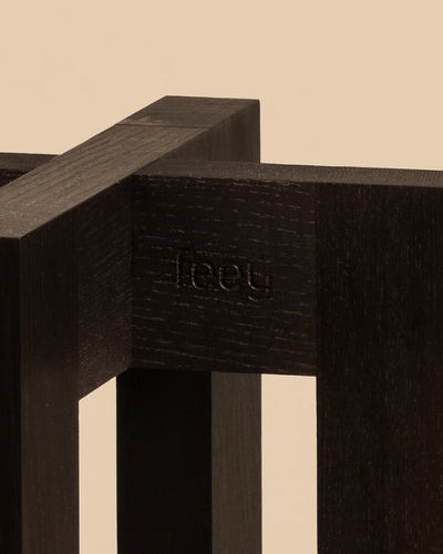 Eine Nahaufnahme einer dunklen Holzstruktur mit minimalistischem Design, auf der „fleey“ eingraviert ist. Dieser elegante Pflanzenständer (Heviton | 25 cm Ø) hebt sich von einem neutralen beigen Hintergrund ab und fügt sich nahtlos in jede stilvolle Umgebung ein.