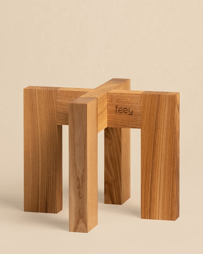 Ein minimalistischer Pflanzenständer aus Holz (Heviton | 25 cm Ø) verfügt über vier ineinandergreifende rechteckige Beine aus poliertem Holz mit eingraviertem „Feety“ auf einer Seite. Der neutrale beige Hintergrund ergänzt jedes Dekor perfekt.
