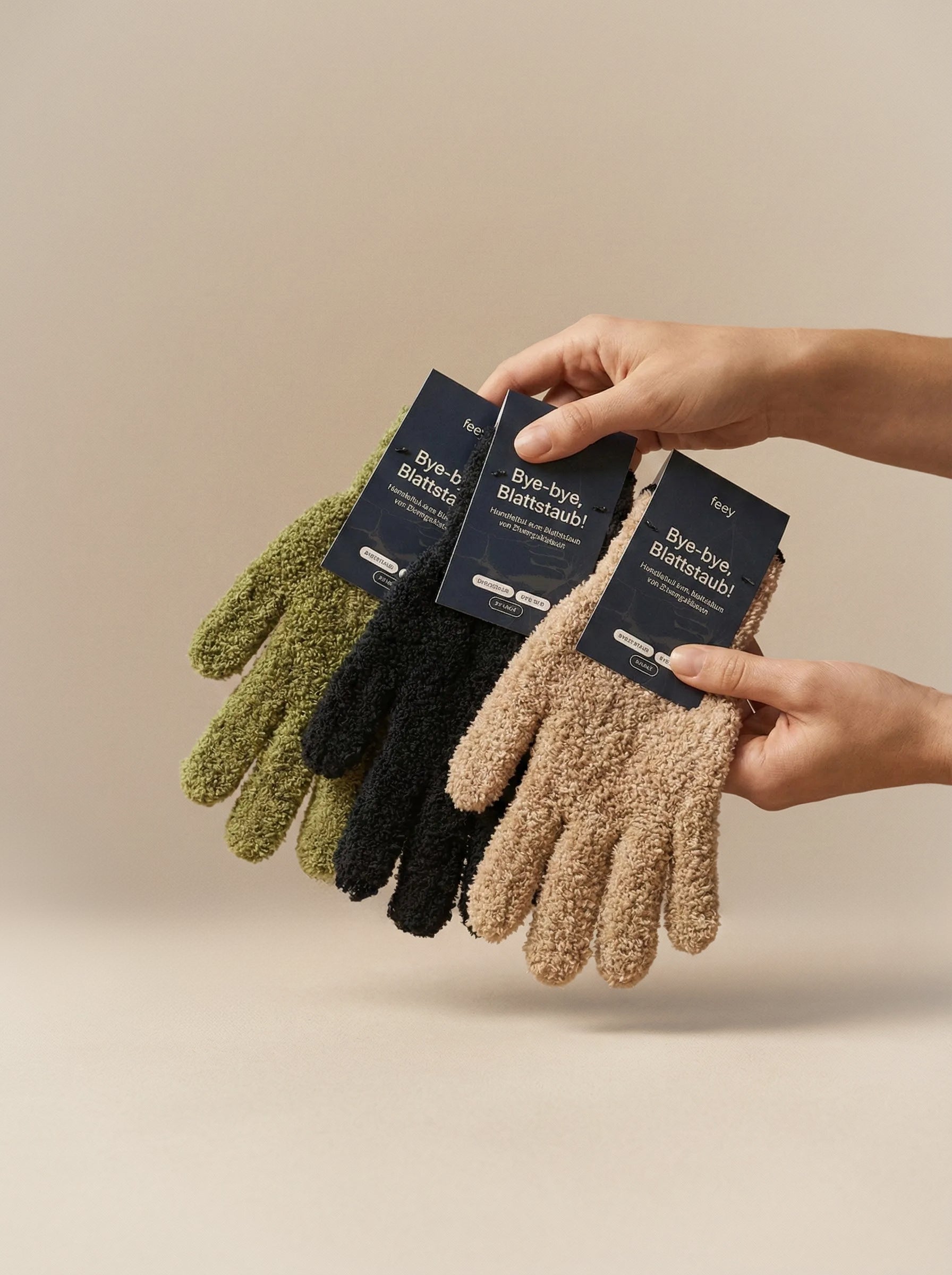 Zwei Hände halten drei Paar Staubhandschuhe in Grün, Schwarz und Beige - jeweils mit der Aufschrift 