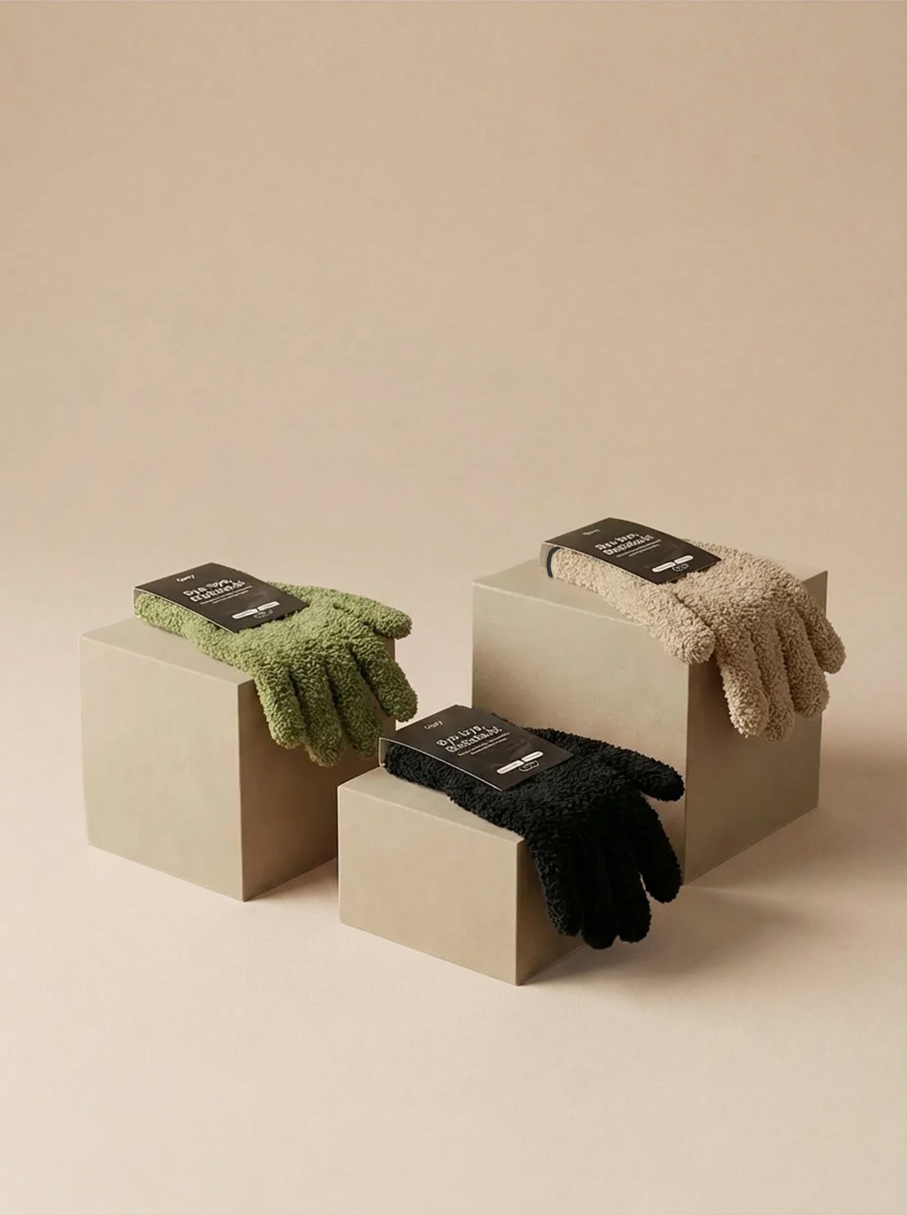 Drei Paar strukturierte Staubhandschuhe - grün, schwarz und beige - werden auf hellbeigen Würfeln vor einem neutralen Hintergrund gezeigt. Jeder Handschuh ist mit einem schwarzen Etikett versehen. Ideal für Zimmerpflanzen Abstauben und Blattstaub entfernen.