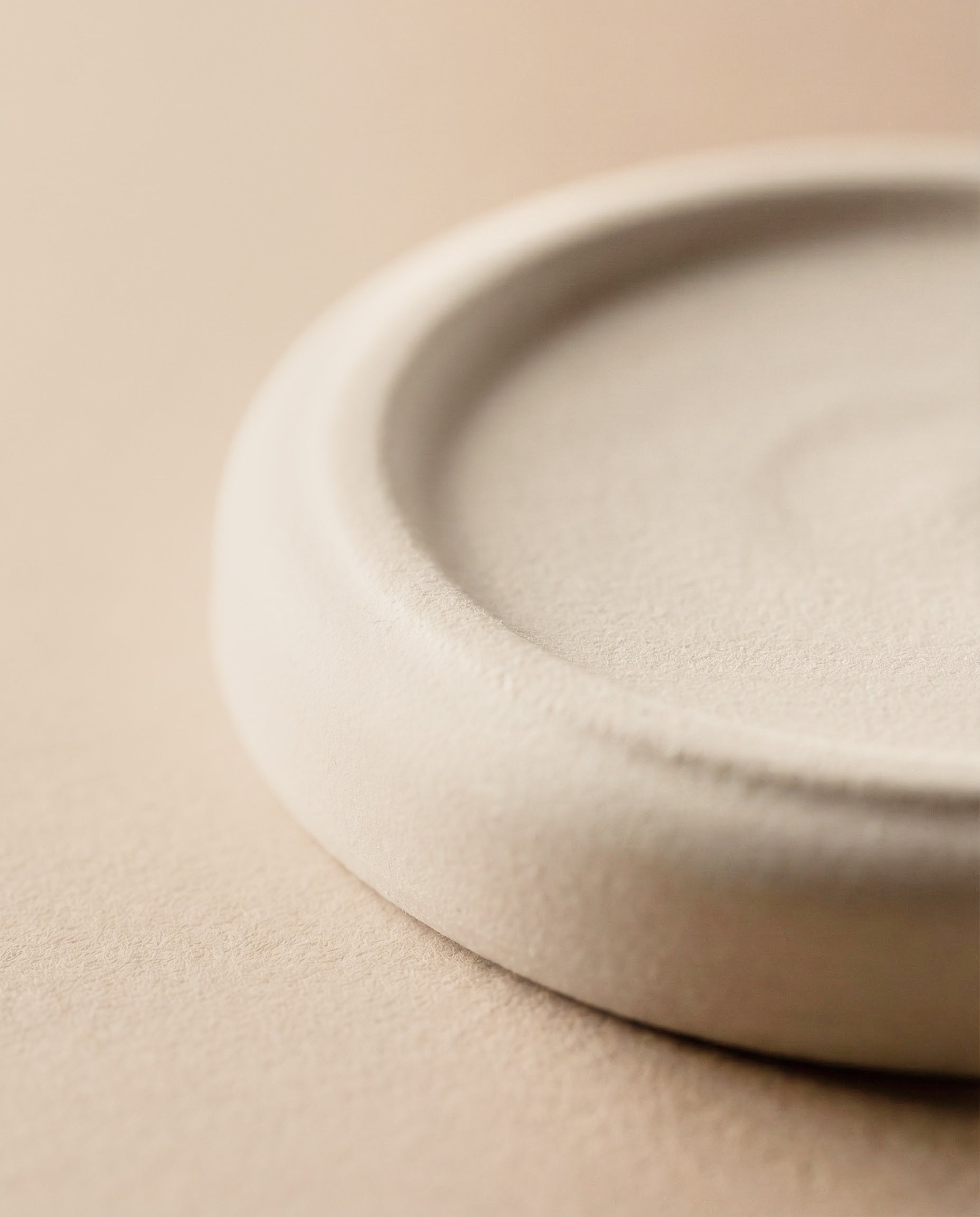 Eine Nahaufnahme der Babypflanzen-Untersetzer aus Keramik (Plattino | 3 Stk.): runde, beigefarbene Untersetzer mit glatter, matter Oberfläche auf neutralem Hintergrund. Der Fokus liegt auf dem Rand und den Schatten - ideal für die Präsentation von Babypflanzen oder Zimmerpflänzchen.