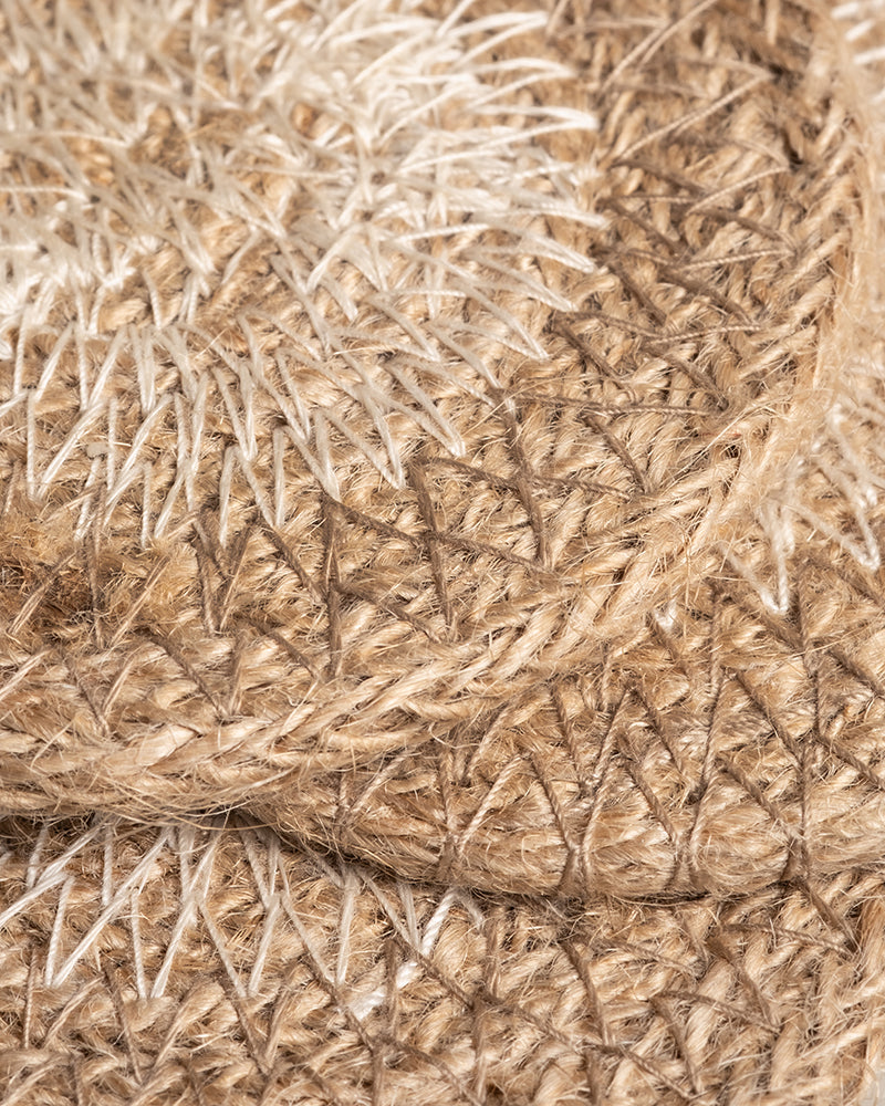 Nahaufnahme von gewebten Strohmatten mit komplizierten Mustern, die dem Babypflanzen-Untersetzer aus Jute ähneln. Die geschichteten Matten mischen helle und dunkle Naturfasern in einem geometrischen Design und erzeugen so ein strukturiertes und organisches Erscheinungsbild.
