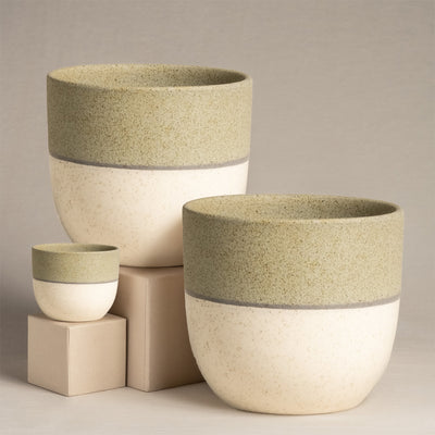Das Keramik-Topfset 'Variado' (2 × 18, 7) umfasst drei handgefertigte Keramiktöpfe in Creme- und Olivtönen. In den Größen klein, mittel und groß sitzt ihre glatte, gesprenkelte Textur elegant auf einer beigen Plattform vor einem neutralen Hintergrund, ideal für exquisite Innendekoration.