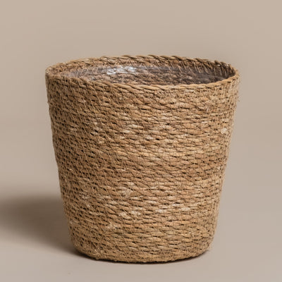 Der Pflanzenkorb aus Seegras (Kesat | 16 cm ⌀) ist ein geflochtener, zylindrischer Korb mit leicht ausgestelltem Rand und sichtbarem, durchsichtigem Kunststoffeinsatz im Inneren, abgebildet auf einem einfarbig beigen Hintergrund.