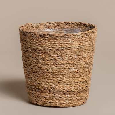 Der Pflanzenkorb aus Seegras (Kesat | 18 cm ⌀) ist ein einzigartiger runder Korb, der aus natürlichem Stroh und Seegras mit einer Kunststoffeinlage gefertigt ist. Er bietet rustikalen Charme und praktische Funktionalität vor einem schlichten beigen Hintergrund.