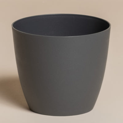 Ein schlichter, dunkelgrauer, zylindrischer Kunststoff-Topf (Kiki | 11 cm Ø) mit leicht ausgestelltem Rand steht auf einer neutralen, beigen Oberfläche - perfekt, um Ihre Pflanzen als stilvolle Wohndekoration in Szene zu setzen.