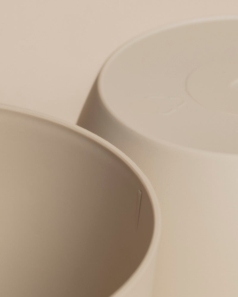 Die Nahaufnahme von zwei beigen Kunststoff-Topf (Kiki | 11 cm Ø) Behältern - einer aufrecht, einer kopfüber - verdeutlicht die glatte, matte Oberfläche und das schlichte Design, ideal für stilvolle Zuhause Deko.