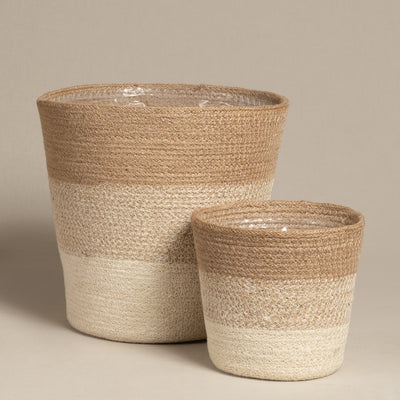 Zwei Pflanzenkorb-Set aus Jute (Lapis | 25, 16) Körbe in Naturtönen stehen nebeneinander, jeweils rund mit einem sanften Farbverlauf von beiger Oberseite nach weißer Unterseite; der größere Korb wird hinter dem kleineren platziert.