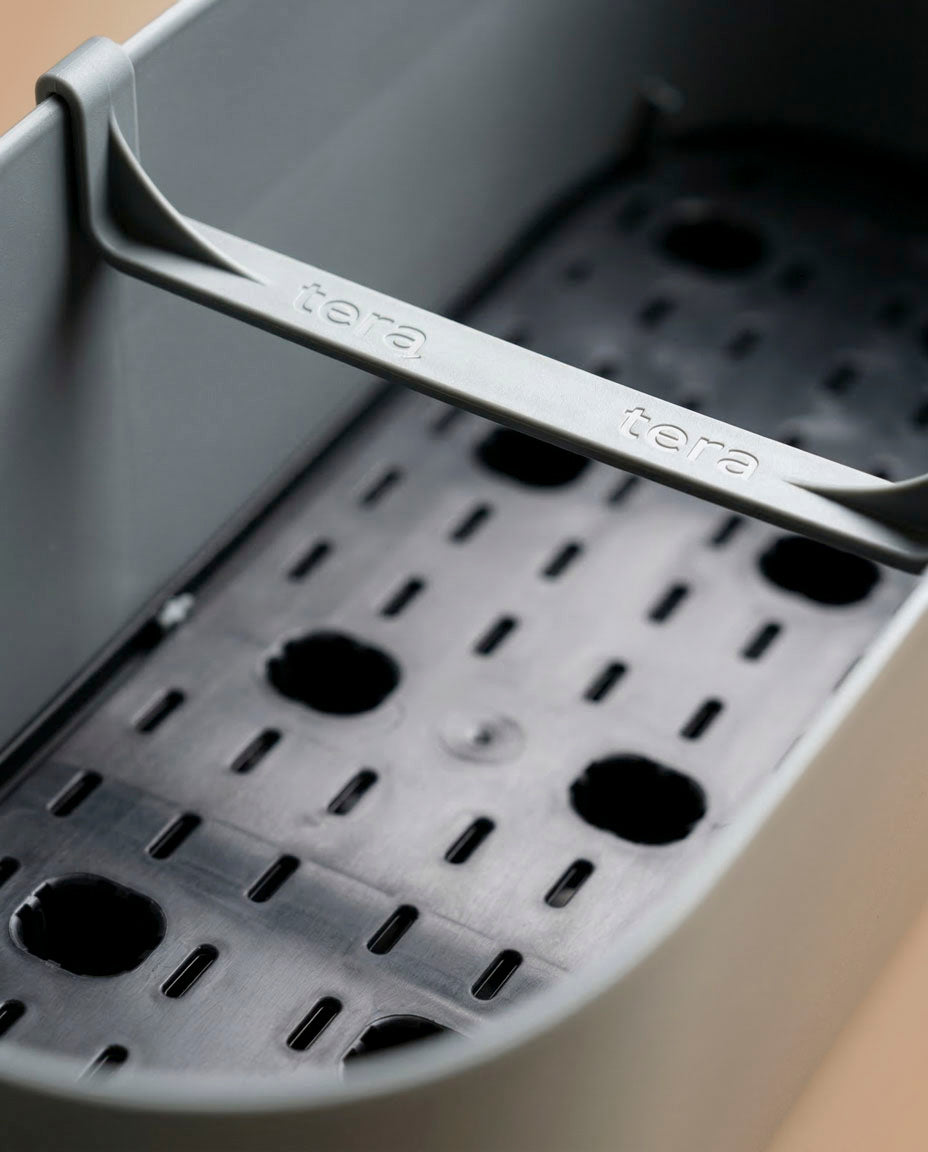 Nahaufnahme eines grauen Pflanzkastens (Paros | 60 cm) mit einem geschlitzten schwarzen Tablett im Inneren und einem 