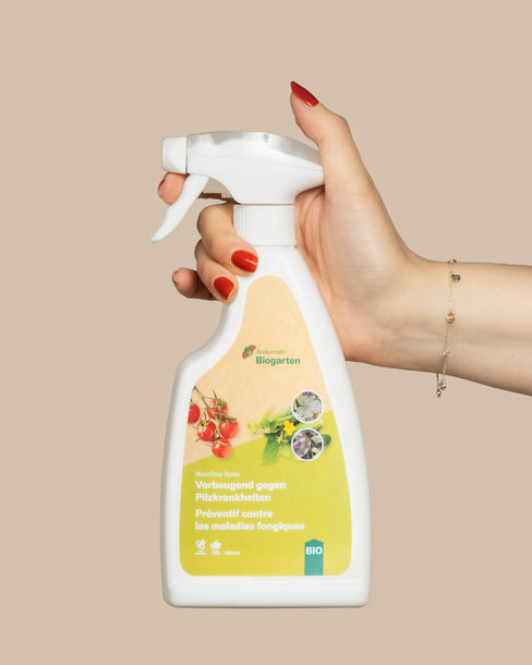 Eine Hand mit roten Nägeln und einem Armband hält eine weiße Sprühflasche mit der Aufschrift 