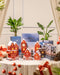 Eine festliche Auslage mit Pflanzen-Adventskalendern in Hausform, verpackten Geschenken mit roten Bändern, grünen Topfpflanzen in Blumentöpfen, Tannenzapfen und einem gemütlichen Vorhang als Hintergrund für eine warme und einladende Szene.