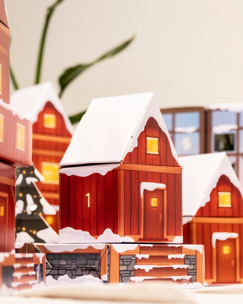 Eine festliche Szene mit einem Papiermodell eines verschneiten, roten Holzhauses mit der Aufschrift 