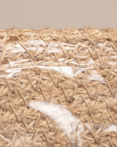 Eine Nahaufnahme des in transparenten Kunststoff eingewickelten Pflanzenkorbs aus Jute (Lapis | 14 cm Ø) zeigt sein kompliziertes Geflecht vor einem neutralen beigen Hintergrund, perfekt für handgefertigte Pflanzenkörbe.