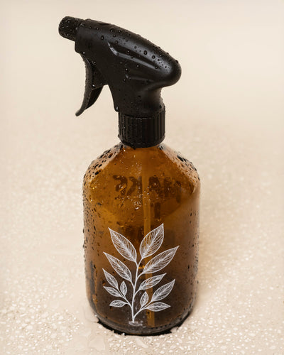 Der Pflanzensprüher aus Glas besitzt einen schwarzen Sprühkopf und ein weißes botanisches Blattmotiv auf der Vorderseite - ideal zum Besprühen von Pflanzen.