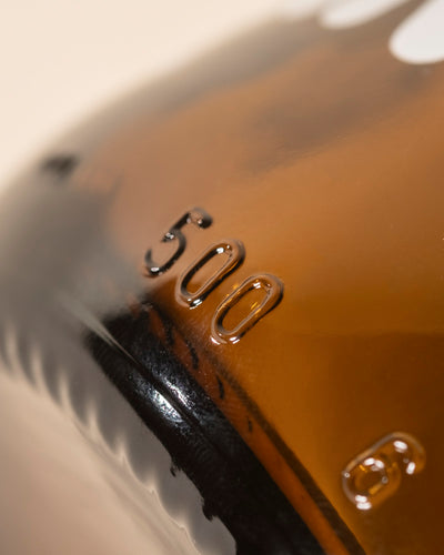 Nahaufnahme des Pflanzensprühers aus Braunglas mit der Prägung "500", mit sanften Lichtreflexen und einem weich verschwommenen Hintergrund - ideal für die sanfte Pflanzenpflege.