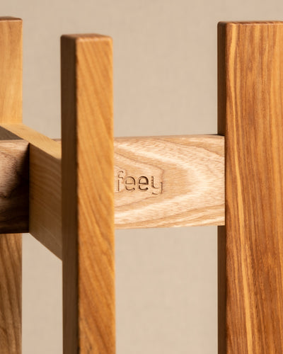 Nahaufnahme eines aus Eschenholz gefertigten Holzstücks mit dem eingravierten Wort „feey“. Die natürliche Oberfläche des Holzes hebt seine reiche Maserung hervor. Dieses einzigartige Design wird vor einem neutralen beigen Hintergrund präsentiert und ist Teil der Pflanzenständer-Kollektion (Stelion | 16 cm Ø).