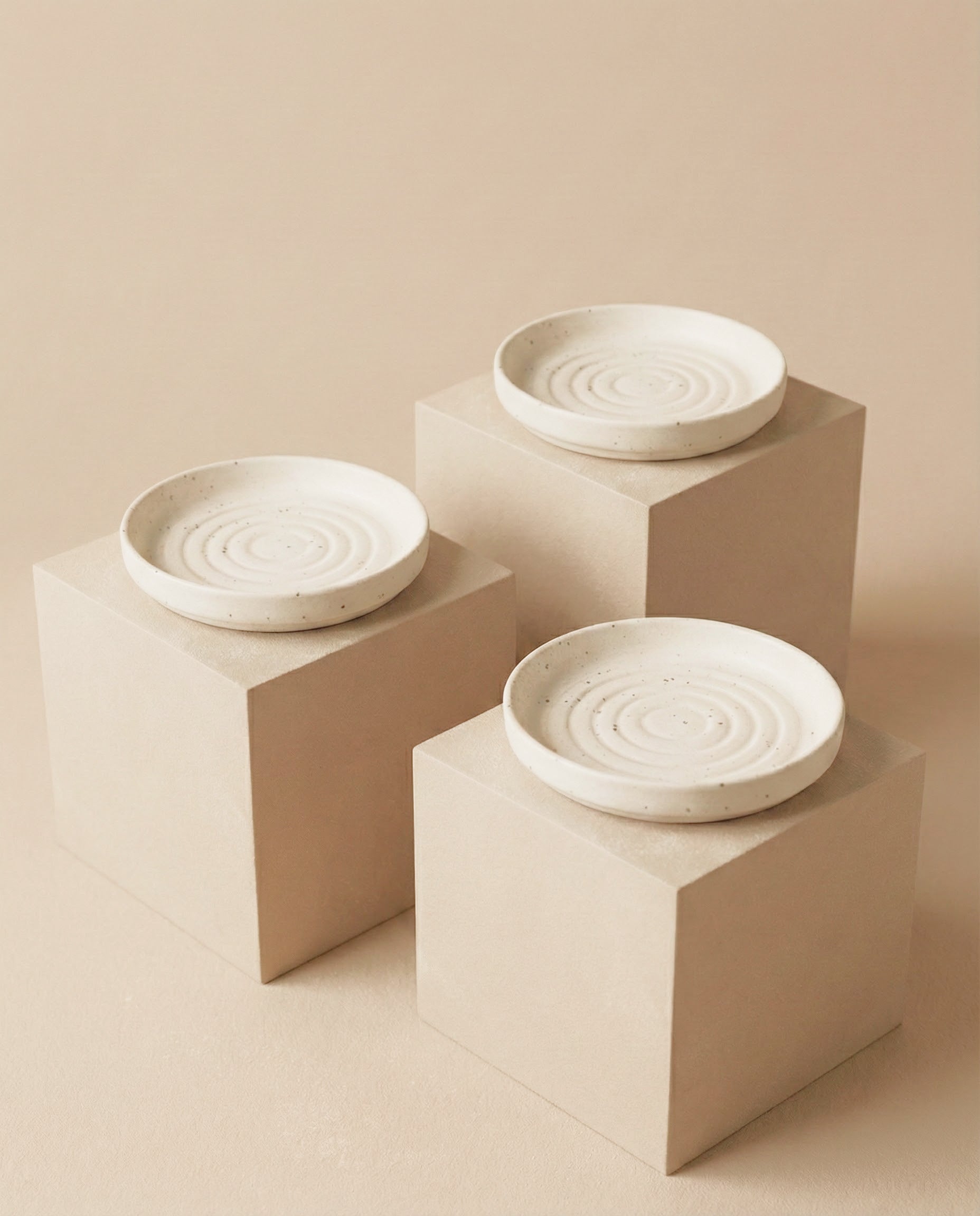 Drei Babypflanzen-Untersetzer aus Keramik (Plattino | 3 Stk.) mit konzentrischen Kreismotiven werden auf beigen, quadratischen Sockeln präsentiert, die vor einem passenden beigen Hintergrund für einen minimalistischen Effekt sorgen.