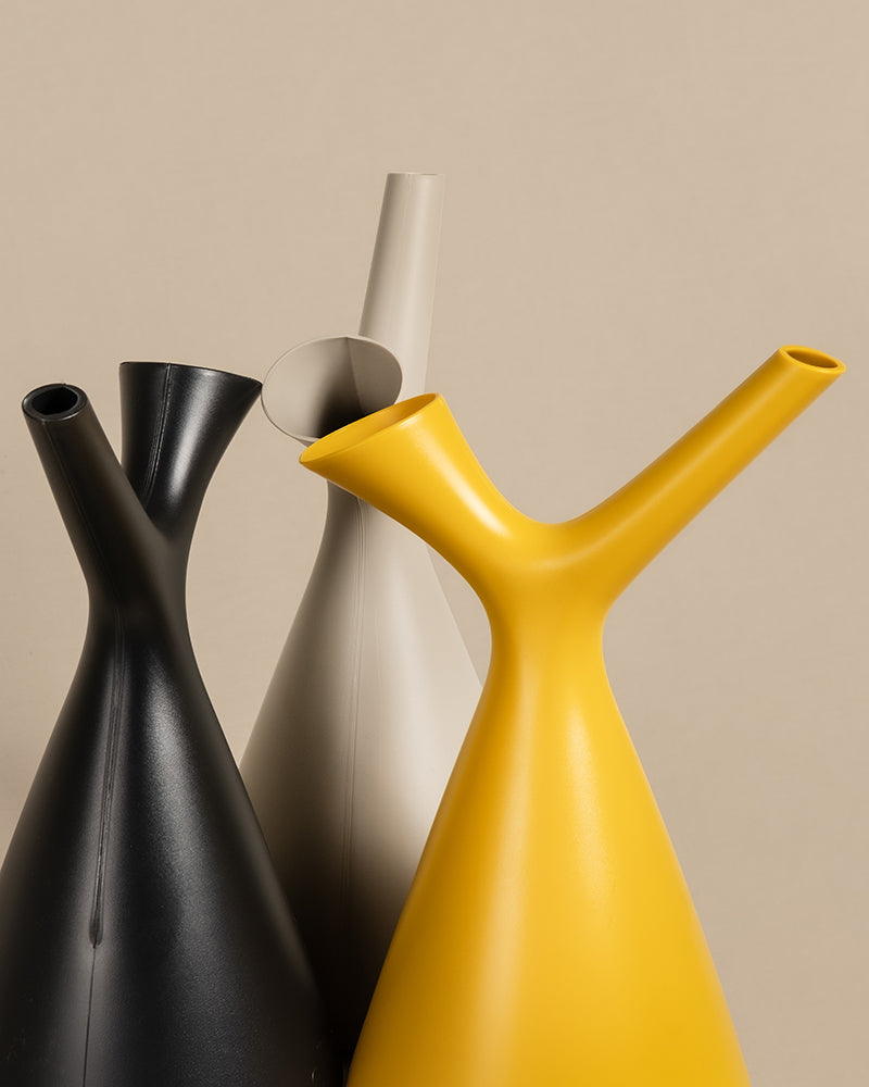 Drei moderne, minimalistische Gießkannen der Plunge-Reihe werden vor einem schlichten beigen Hintergrund präsentiert. Die Kannen sind schlank, haben längliche Ausgießer und sind in schwarzem, weißem und gelbem Polypropylen erhältlich, dicht beieinander angeordnet.